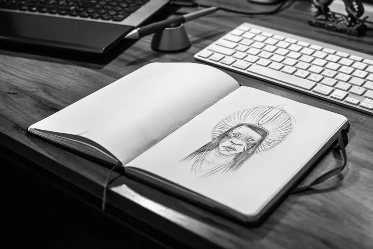 An open sketchbook with a pencil portrait beside a keyboard on a wooden desk (stock photo)