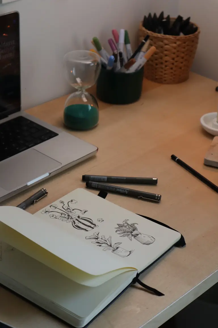A desk with a sketchbook, pens and a laptop