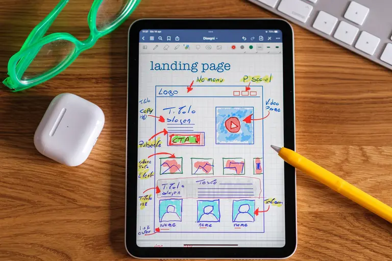 A tablet showing a hand-drawn landing page wireframe beside a pencil