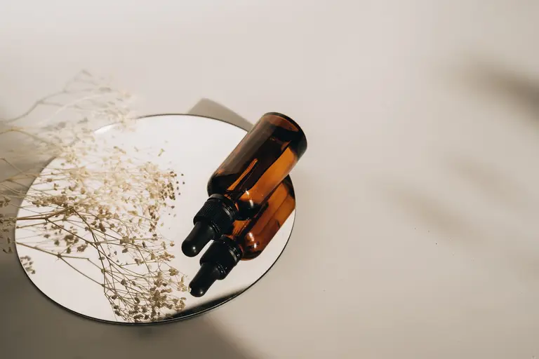 A brown dropper bottle and dried flowers on a round mirror