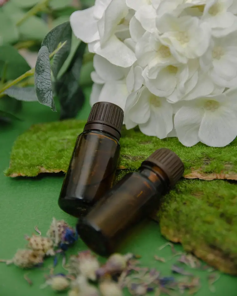 Amber essential-oil bottles on moss beside white hydrangea flowers