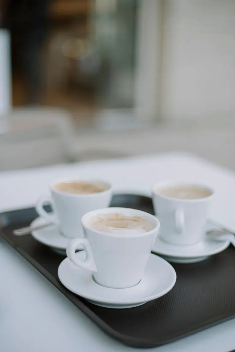 Three white cups of coffee on a dark tray