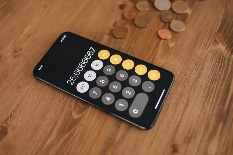 A smartphone showing a calculator on a wooden table beside coins