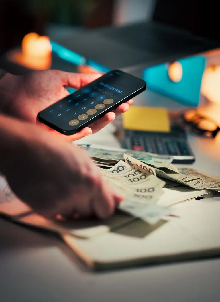 Hands using a phone calculator beside banknotes and a notebook