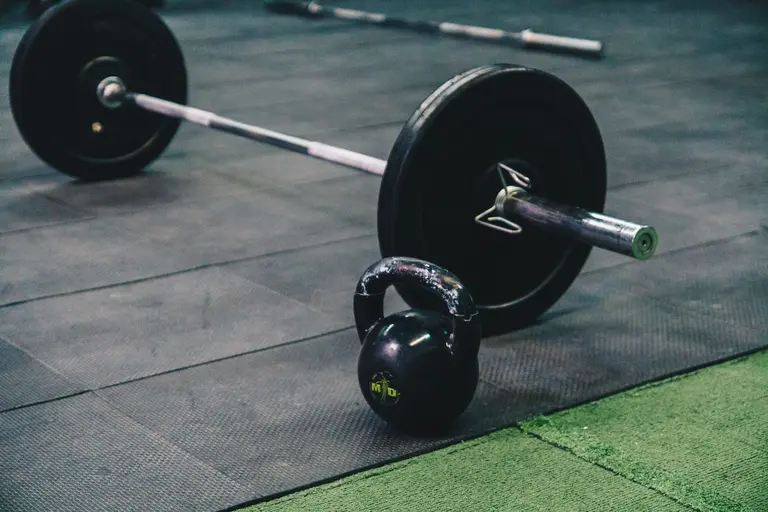 A barbell and kettlebell on a black rubber gym floor