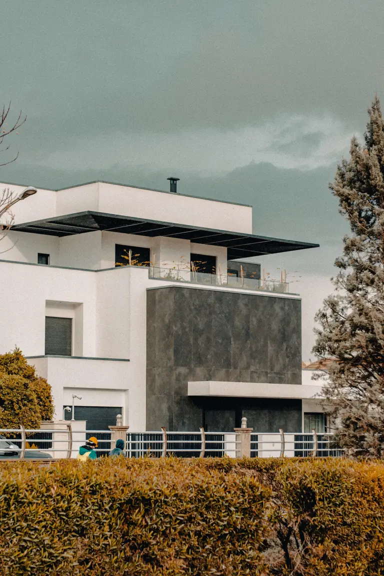 A contemporary white house with a dark stone facade seen over a hedge