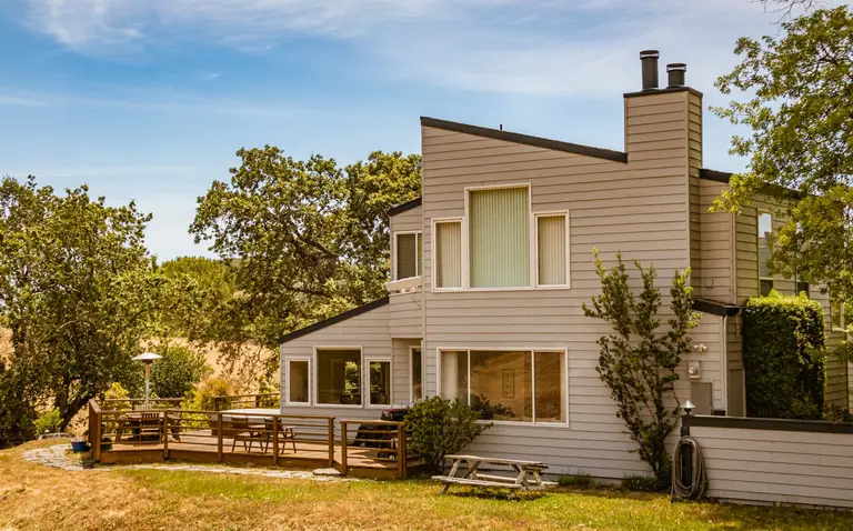 A wooden-clad house with a deck and trees in the garden