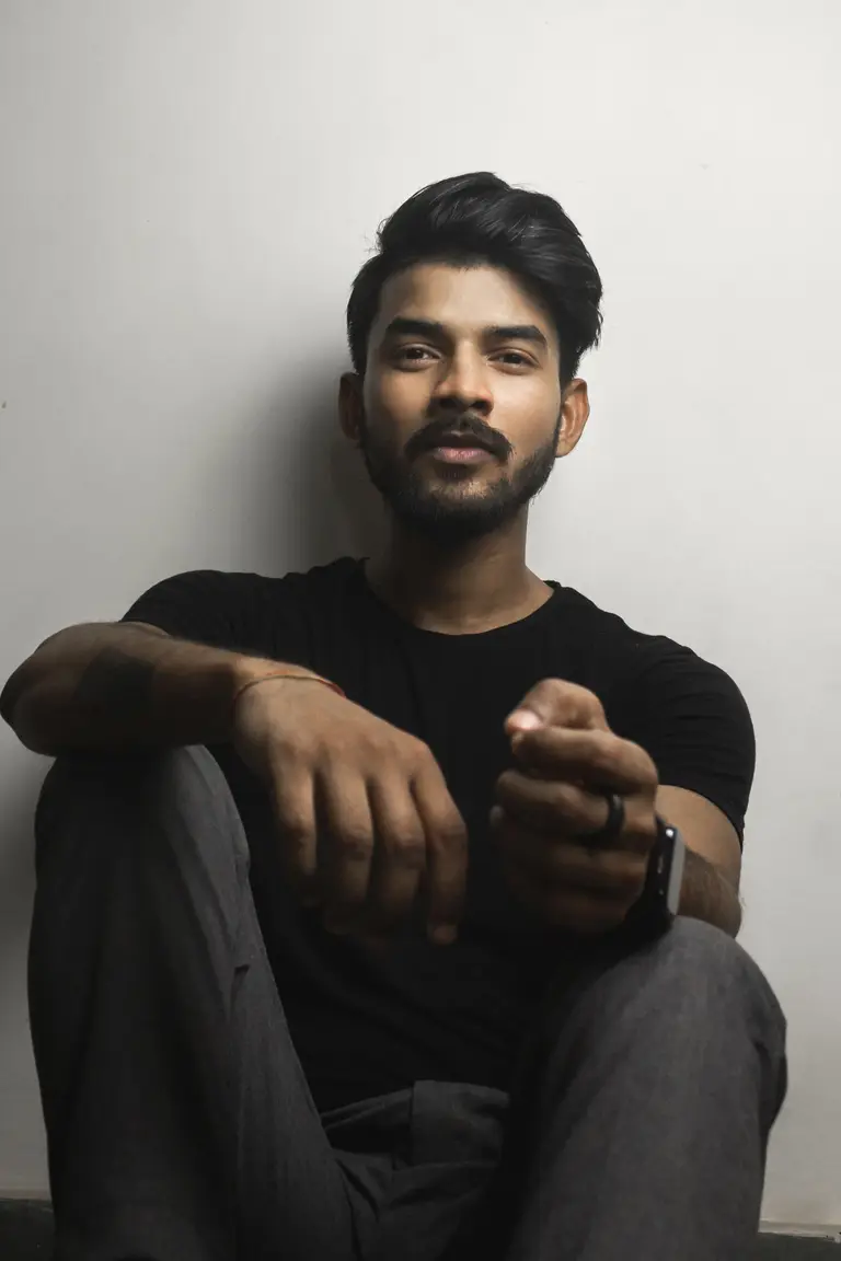 A bearded man in a black shirt sitting against a wall, used as the fictional designer Aarav Sen (stock photo)