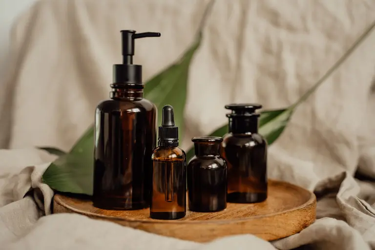 Unbranded amber glass skincare bottles on a wooden tray with a green leaf, representing the Aurora Botanics brand identity