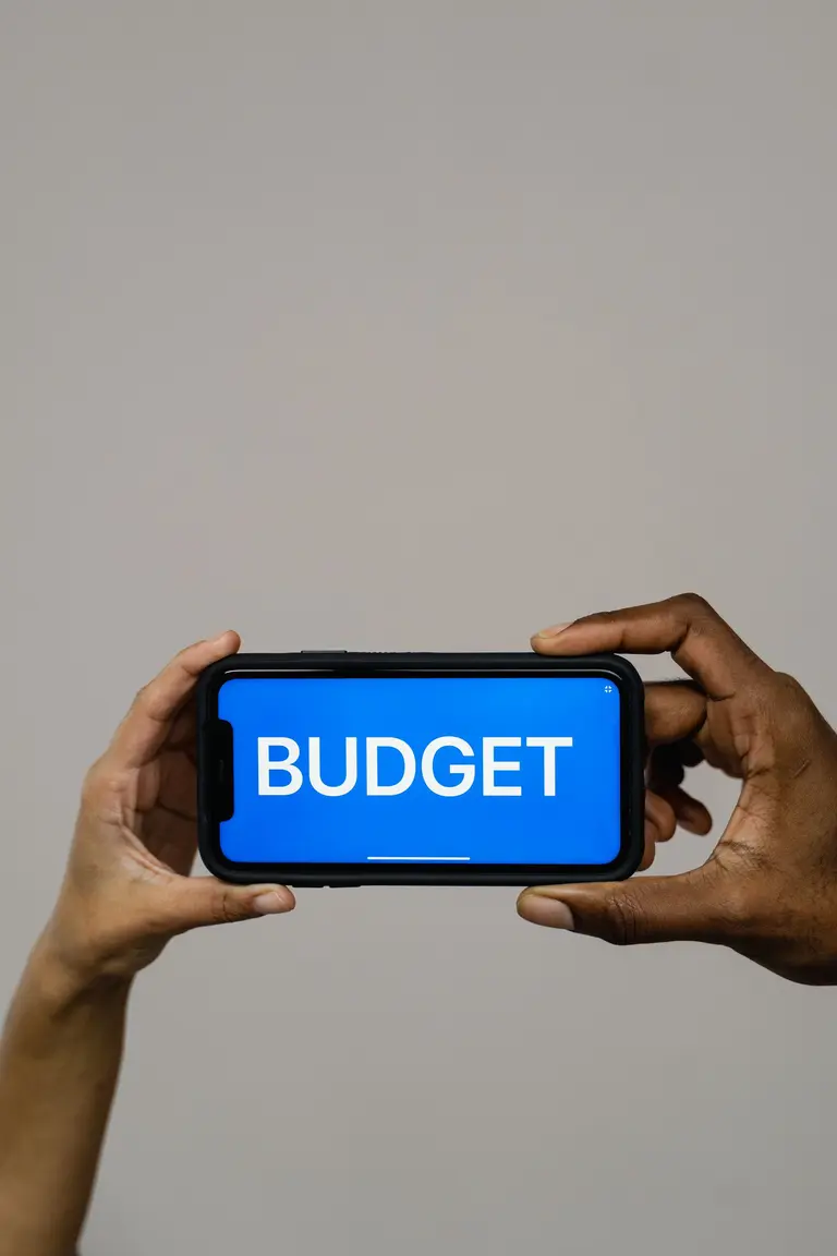 Hands holding a smartphone that shows the word BUDGET on a blue screen, representing the Ledgerly app