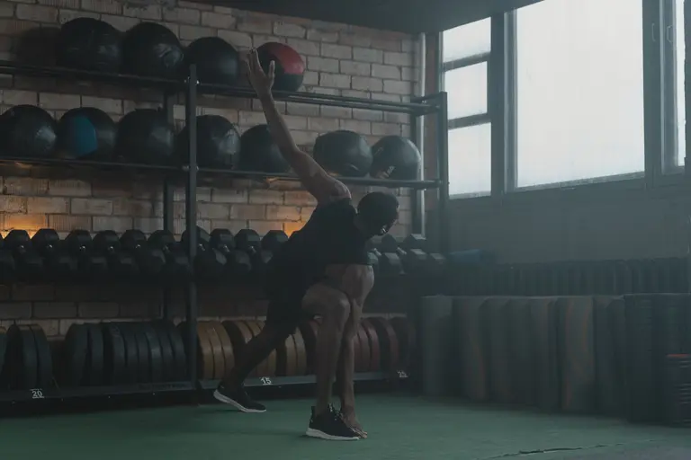 An athlete stretching in a gym beside racks of medicine balls, representing the PulseFit workout app